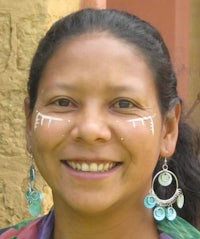 a woman with a white face and blue earrings smiles