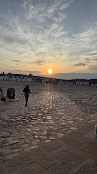 the sun is setting behind a group of people on a cobblestone street
