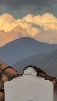 a cloudy sky over a house with a mountain in the background